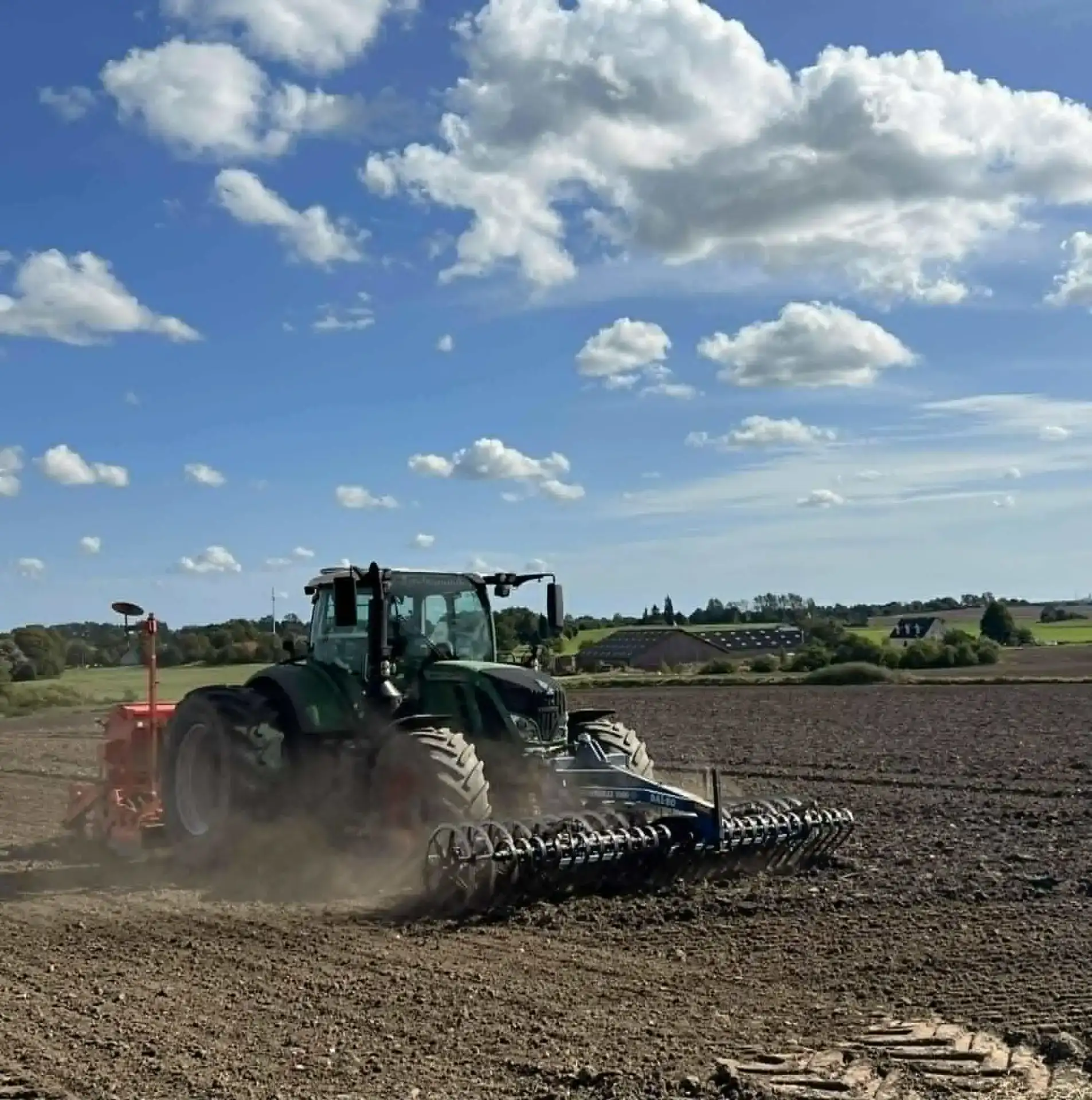 Landbrugs- og entreprenørmaskine arbejder på marken under en klar himmel.