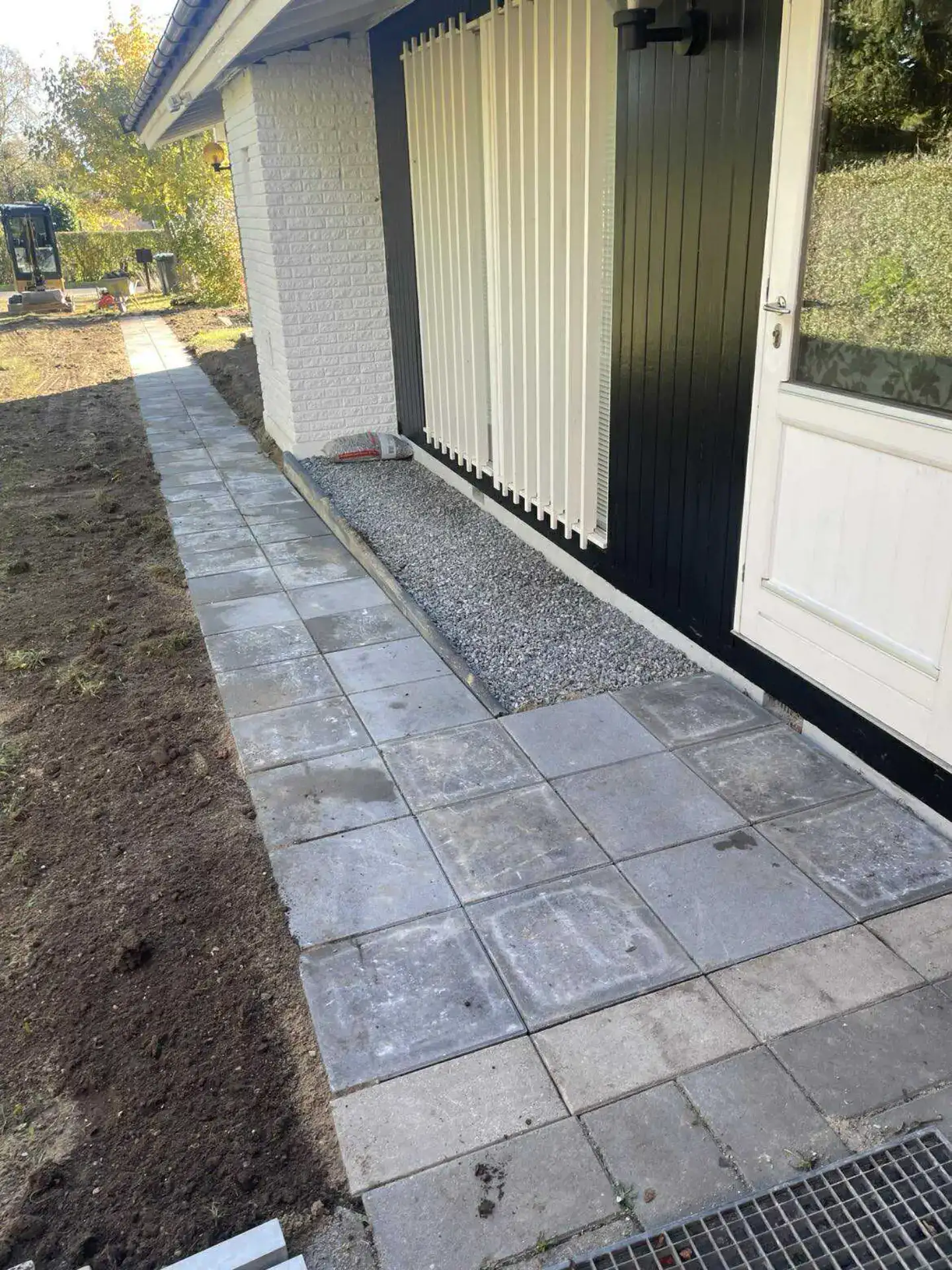 Højkvalitets flisebelægning foran hus med hvid og sort facade, perfekt til udendørsarealer.
