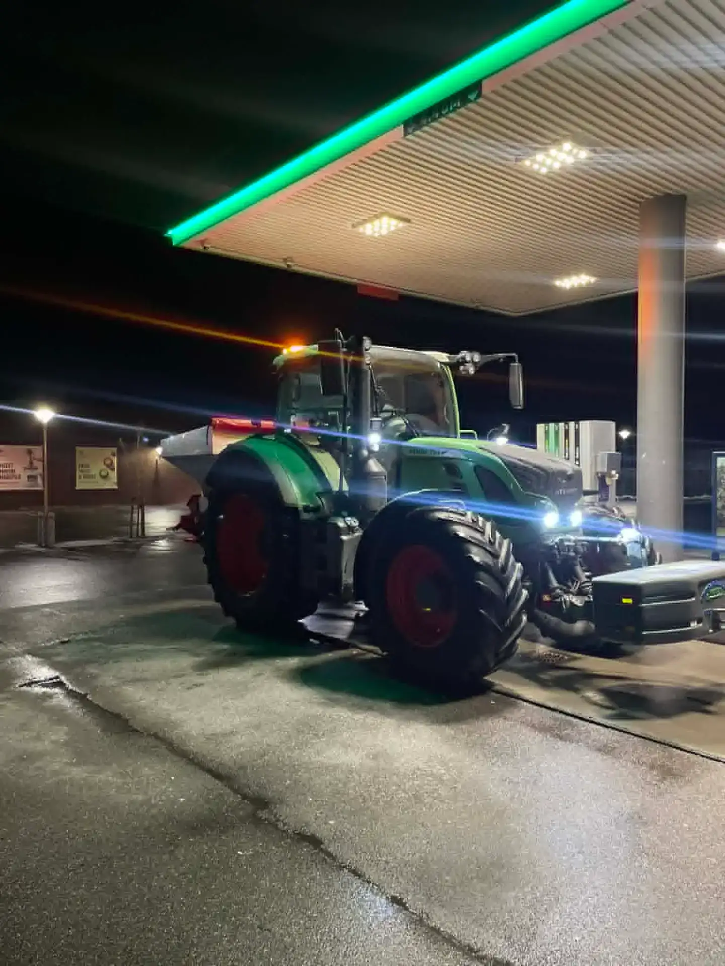 Traktor ved tankstation under natten med farvet lys.